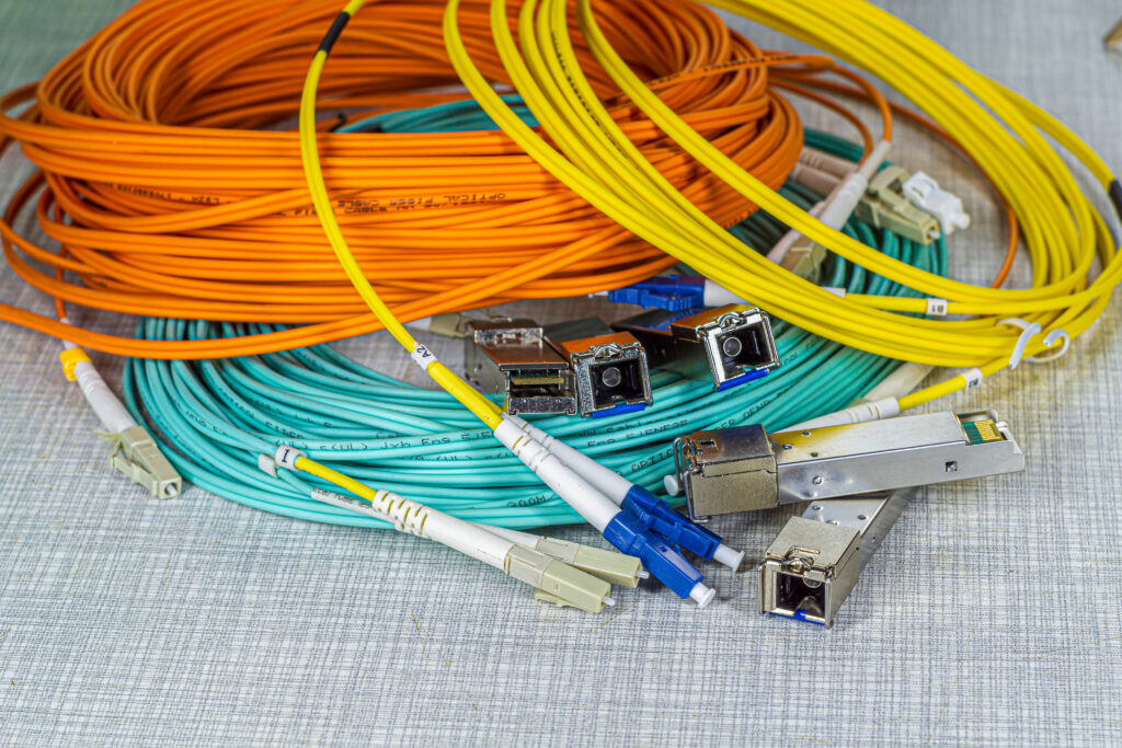 close up side view of orange, yellow, cyan coloured optical cables coiled into a ring with connectors and and 5 sfp (small form factor pluggable)
